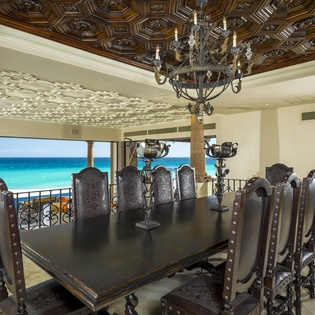 Gather around this grand dining table where ornate chandeliers illuminate meals with breathtaking turquoise ocean views as your backdrop.
