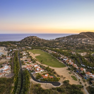 Stunning coastal community with golf course, beaches, and hillside homes captured at golden hour.