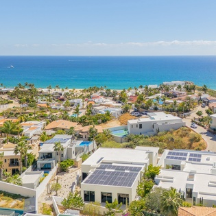 Stunning aerial view of beachfront community with modern vacation homes nestled between tropical palms and pristine turquoise waters.