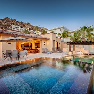 Luxurious villa with sparkling pool, covered outdoor dining, and dramatic mountain backdrop—perfect for evening gatherings under the stars in your private desert oasis.