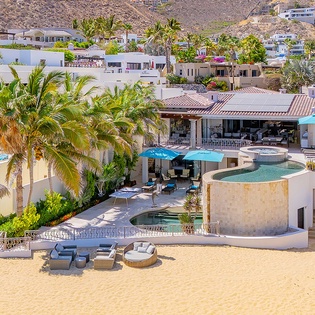 Hillside beachfront villa showcasing multi-level pools, private sandy beach access, tropical palms, and sunny outdoor lounging areas in an exclusive coastal neighborhood.