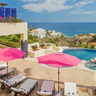 Lounge poolside under vibrant pink umbrellas with sweeping ocean views and a luxurious hot tub, all set on a spacious sun-drenched terrace perfect for your escape.