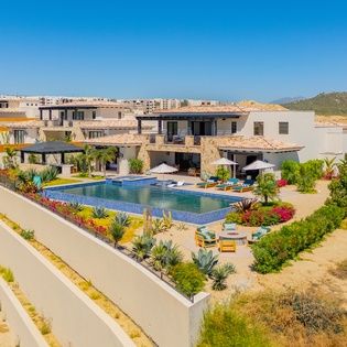 Stunning aerial view of a modern villa featuring a sparkling pool surrounded by vibrant landscaping in a hillside development.
