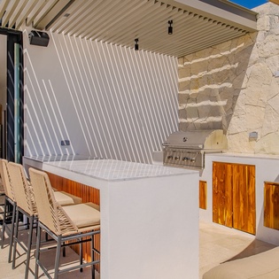 Your private outdoor kitchen awaits with sleek bar seating and professional grill, perfect for sunset entertaining under elegant pergola shade.