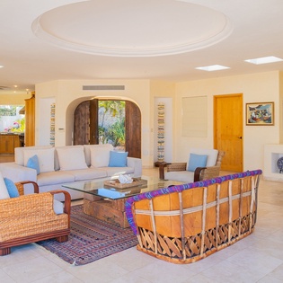 Relax in your spacious living room with soaring ceilings, natural wicker furnishings, and tropical garden views through elegant arched doorways.