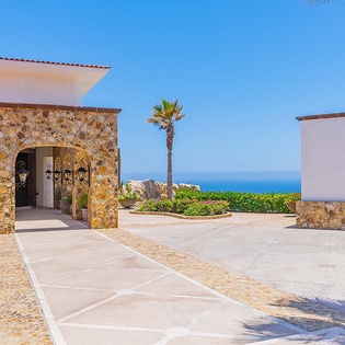 A welcoming entrance framed by warm stone archways opens onto a spacious courtyard with sweeping ocean vistas. The tranquil setting blends coastal charm with Mediterranean elegance, setting the tone for a memorable stay.