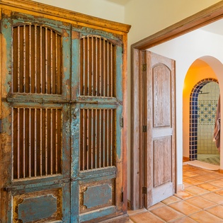 Step into a charming space where rustic meets elegance. Weathered turquoise doors and warm terracotta floors create an inviting atmosphere, while the arched entryway beckons you to explore further.
