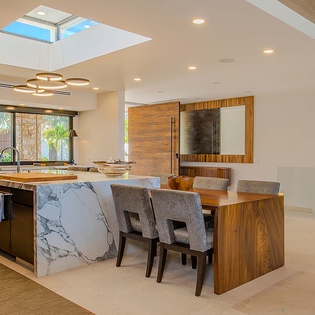 Gather around a stunning dining and kitchen space where natural light floods in through a dramatic skylight overhead, highlighting rich wood tones and marble accents perfect for your morning coffee or evening meals.
