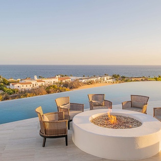 A stunning infinity pool overlooks the sparkling coastline, framed by an elegant circular fire pit surrounded by plush seating—your perfect spot to unwind as the sun dips below the horizon.