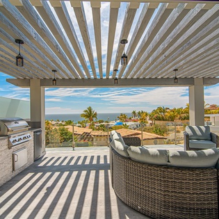 Relax in your private outdoor kitchen oasis with stunning ocean views and comfortable seating under a modern pergola.