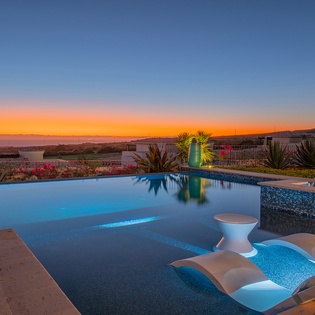 Stunning infinity pool captures breathtaking sunset views over coastal landscape with tropical gardens and distant mountains.