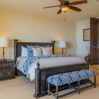 Your elegant bedroom features a handcrafted wooden four-poster bed with crisp blue linens, bedside lamps, and a ceiling fan for comfort.