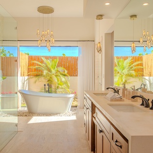 Your luxurious master bathroom features a stunning freestanding tub beneath elegant pendant lights, where you'll unwind with tropical garden views.