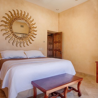 Your serene bedroom features crisp linens, a striking sun-burst mirror, and warm golden walls that create a peaceful sanctuary for rest.