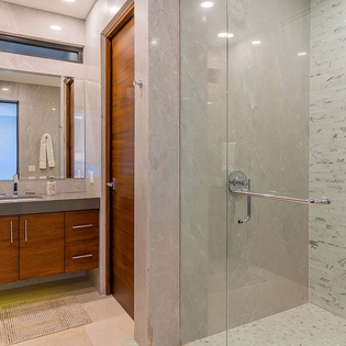 Sleek, spa-like bathroom features a spacious walk-in shower with marble-style tiling and a modern vanity with warm wood cabinetry to make you feel refreshed.