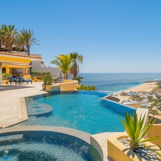 Stunning infinity pool overlooking azure waters and golden coastline, surrounded by tropical palms and luxurious outdoor lounging spaces.