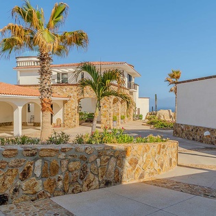 Mediterranean-style villa exterior featuring stone accents, terracotta roofs, and lush palm trees set against a scenic coastal backdrop.