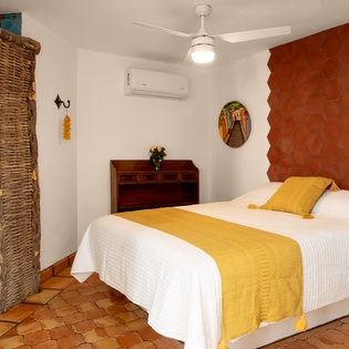 Unwind in your vibrant Mexican-inspired bedroom featuring a comfortable bed, air conditioning, and unique artistic touches for a restful stay.