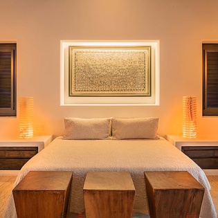 Slip into a serene bedroom where ambient lighting casts a warm, welcoming glow. Rest easy beneath soft linens on your plush king bed, flanked by decorative wooden accents and soothing lamps that set the perfect mood for relaxation.