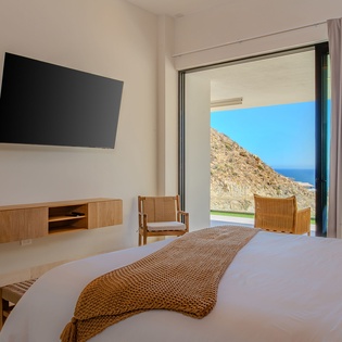 Your serene bedroom opens to stunning mountain and sea views, with modern comforts and warm textures creating the perfect retreat.