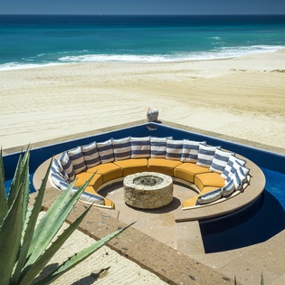 Stunning beachfront property featuring a circular fire pit seating area with direct ocean access and pristine sandy beach.