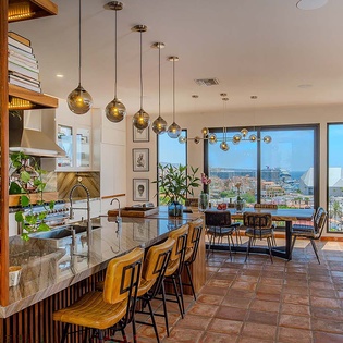 Sweeping ocean views frame your open-concept living space, where modern pendant lighting and lush greenery create an inviting atmosphere for memorable meals and relaxed evenings together.