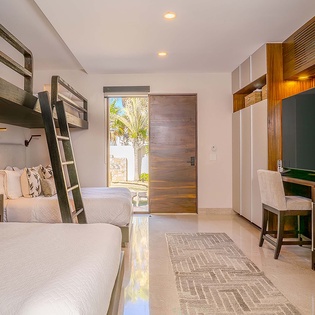 Step into your stylish retreat where natural light floods through the door, revealing glimpses of paradise. Bunk beds maximize space while the modern desk and entertainment setup ensure both work and relaxation blend seamlessly in your coastal haven.