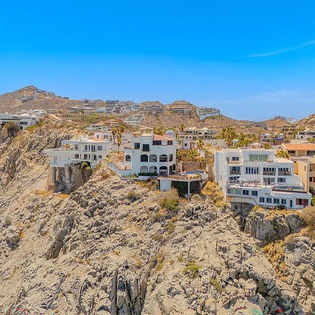 Hillside coastal community with modern villas perched on dramatic rocky cliffs beneath clear blue skies, showcasing the striking desert-meets-ocean landscape surrounding the property.