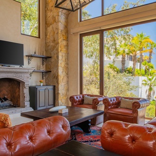 Sink into rich leather seating by your stone fireplace while ocean views and palm trees frame your coastal sanctuary through soaring windows.