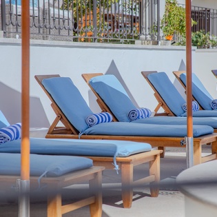 Sink into plush blue loungers with rolled towels, where your perfect poolside afternoon awaits under the warm sun.