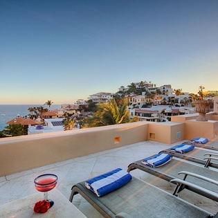 A stunning coastal hillside community overlooking calm blue waters, framed by palm trees and white-washed architecture in the golden hour light.