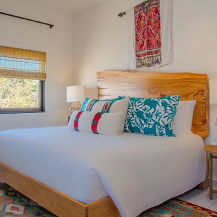 Sink into your cozy bed surrounded by vibrant textiles and natural light streaming through bamboo shades.