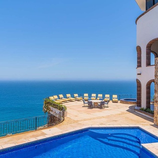 Stunning clifftop villa with private pool overlooking endless blue waters. Stone-clad architecture frames your sun-drenched terrace, where lounge chairs invite pure relaxation beneath the open sky.