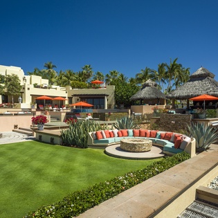 Luxurious beachfront resort showcases modern architecture, tropical landscaping, and thatched-roof dining pavilions under brilliant blue skies.