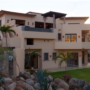 Modern beachfront villa features multiple levels with spacious terraces, lush tropical landscaping, and warm ambient lighting at dusk—ideal for a memorable coastal getaway.
