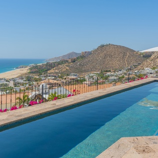 Stunning infinity pool overlooking the coastline with panoramic mountain and ocean views during daylight hours.