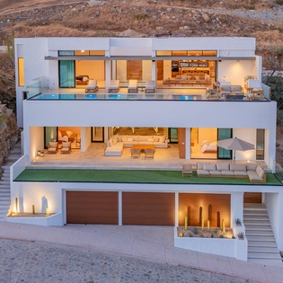 A stunning modern villa showcases contemporary architecture with multiple terraces, pool, and seamless indoor-outdoor living spaces set in natural desert landscape.