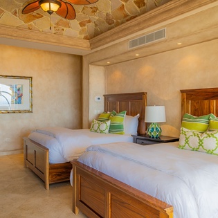 Rest peacefully in your elegant twin bedroom featuring rich wood furnishings and vibrant green accents under beautiful stone ceiling details.
