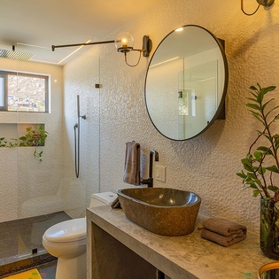 Step into your serene, spa-like bathroom with textured walls, a rustic stone vessel sink, and warm lighting. Fresh greenery and soft towels create a welcoming retreat for your getaway.