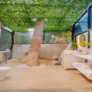 Unwind in your private outdoor bathroom oasis, where tropical ivy cascades overhead and natural stone meets modern luxury beneath open sky.