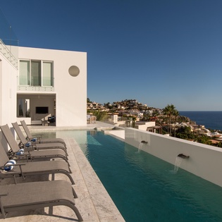 Modern white villa with infinity pool overlooking the Mediterranean coastline and hillside village.