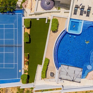 This property offers a vibrant tennis court and a beautifully shaped pool with sun loungers, surrounded by manicured lawns and modern outdoor design.
