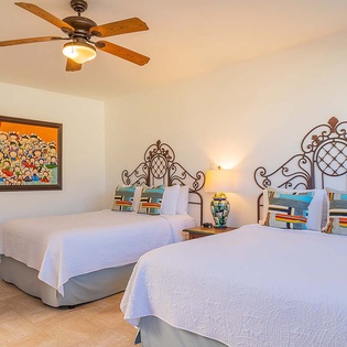 Unwind in your bright, spacious bedroom featuring two plush beds with vibrant throw pillows, charming local artwork, and a gentle ceiling fan for ultimate comfort.