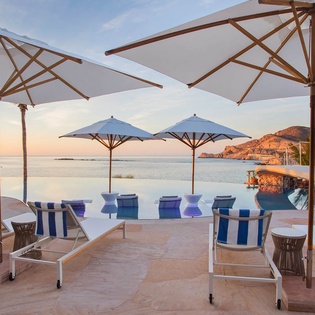 Lounge in style by the infinity pool, where calm waters mirror the sunset and panoramic sea views stretch toward distant coastal hills.