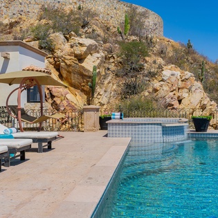Your private pool sanctuary beckons with crystal-clear waters and comfortable loungers, perfectly framed by stunning desert rock formations under endless blue skies.
