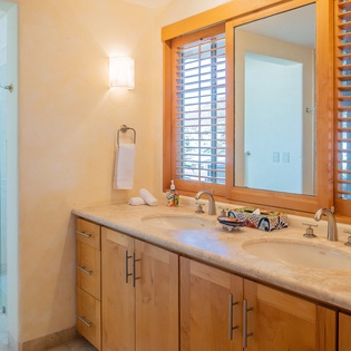 Step into your elegant bathroom with double vanity sinks, natural wood cabinetry, and tropical shutters filtering warm light.