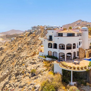 Stunning coastal villa perched on dramatic cliffs, featuring a private pool overlooking golden beaches and turquoise waters in a serene hillside setting.
