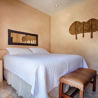 Relax in your serene bedroom featuring a plush bed dressed in soft white linens, warm earthy tones, unique artisan wall décor, and tile floors that keep you cool on warm tropical nights.