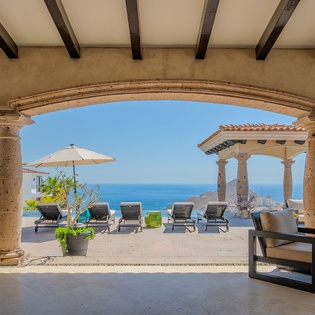 Step onto your private terrace where stunning ocean views stretch endlessly beyond elegant stone columns and comfortable lounge seating.