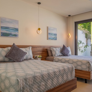 Unwind in your serene twin bedroom with elegant ocean artwork and peaceful courtyard views through floor-to-ceiling windows.